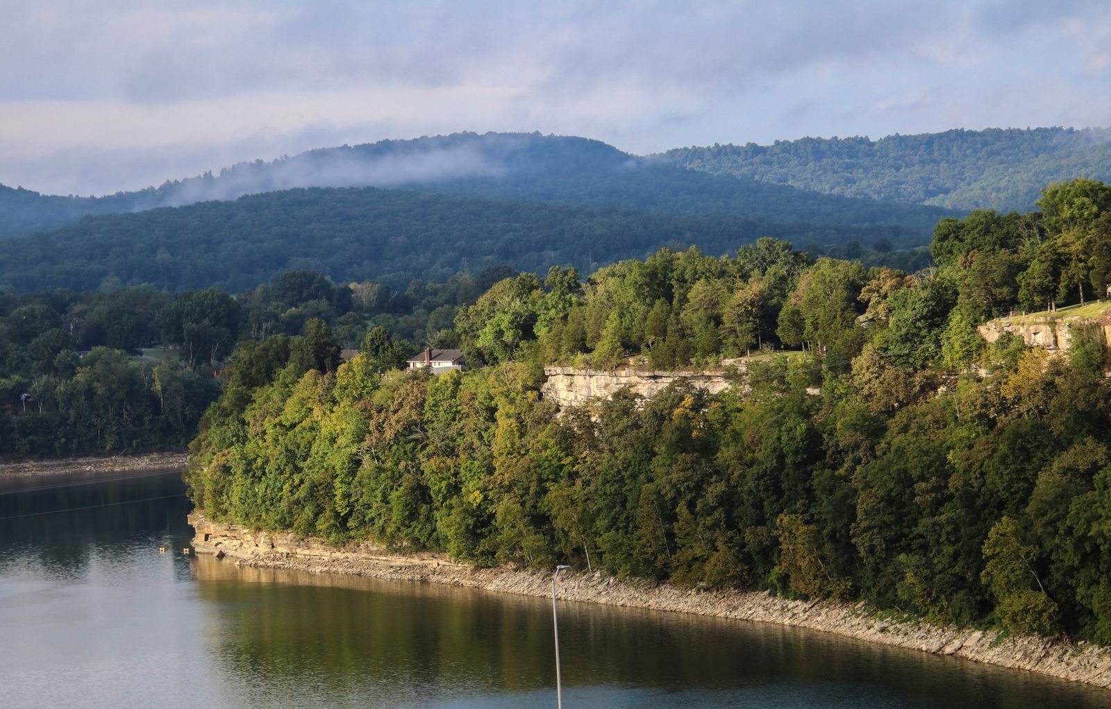 Wooded Ozark hills and limestone bluffs rising above a calm lake under a soft sky
